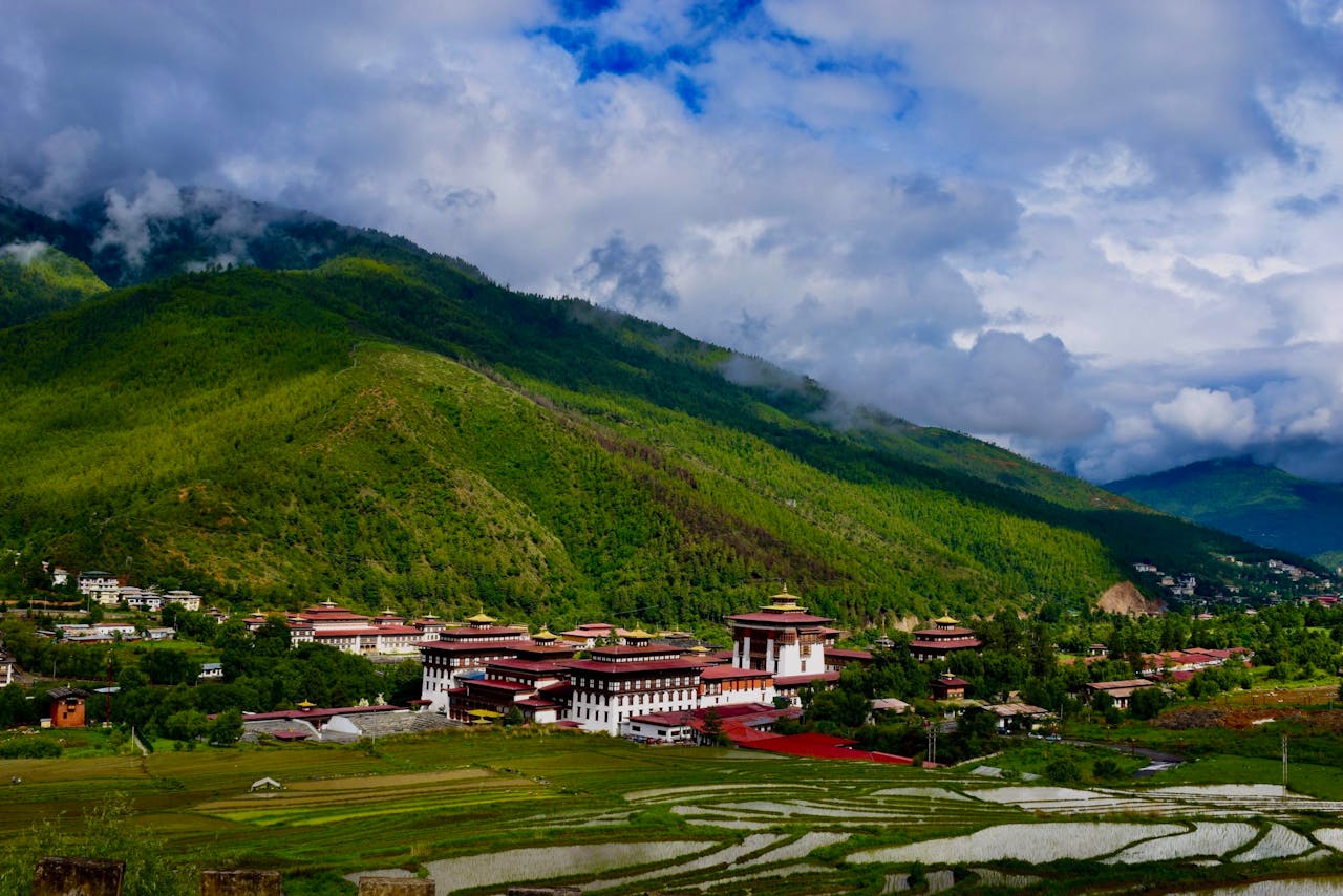 home-hero A breathtaking view of the Tashichho Dzong in Thimphu valley, surrounded by lush green mountains under a cloudy sky.